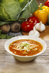 Bowl of tomato soup and fresh vegetables on old wooden table