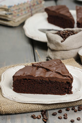 Chocolate cake on white plate, on hessian. Coffee beans on woode