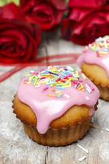 Muffins covered with pink icing and colorful sprinkles on wooden