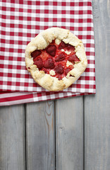 Strawberry tart on checked red and white table cloth on grey woo