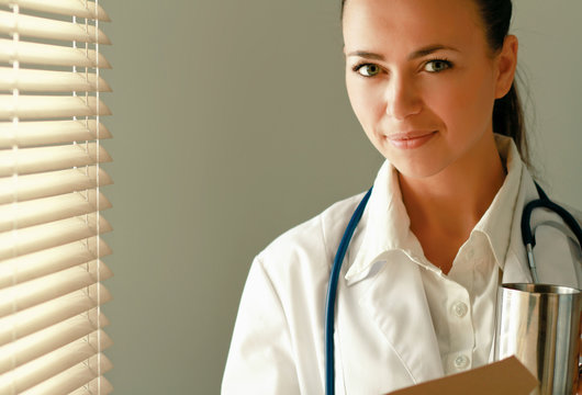 Woman  doctor near window with folder and holding cup