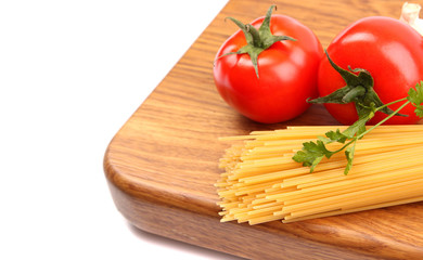 uncooked spaghetti, garlic and tomatos on a board