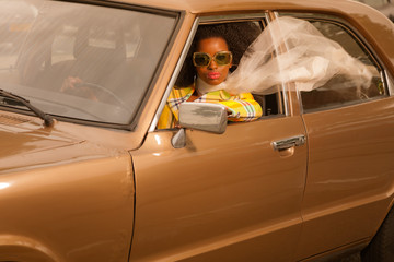 Vintage 70s fashion afro woman with sunglasses driving in brown - obrazy, fototapety, plakaty