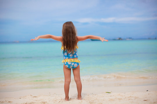 Beautiful little girl spread her arms standing at the beach