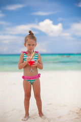 Little girl drinks juice from watermelon on the exotic beach