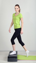 Beautiful young woman exercises on stepper
