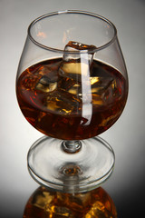 Brandy glass with ice on grey background
