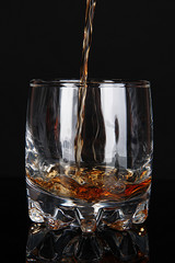 Brandy pouring into glass on black background