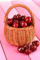 Cherry berries in wicker basket on wooden table close-up