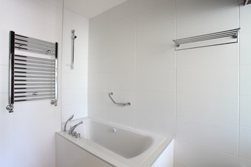 Bathtub, heated towel rail and shelf in bathroom.