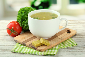 Cup of soup with bouillon cubes on wooden table