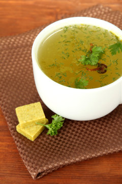 Cup of soup with bouillon cubes on wooden background