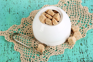 Unrefined sugar in white sugar bowl on wooden background