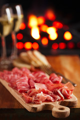 Platter of serrano jamon Cured Meat with cozy fireplace and wine