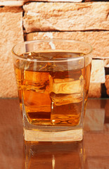 Glass of whiskey and ice on brick wall background