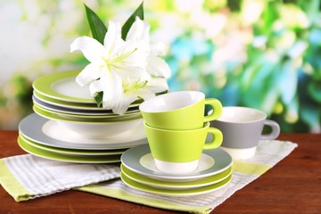 Empty plates and cups on wooden table on green background