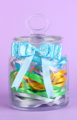 Glass jar containing various colored ribbons on lilac