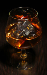 Brandy glass with ice on wooden background