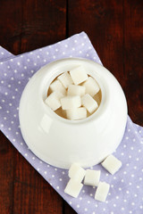 Refined sugar in white sugar bowl on wooden background