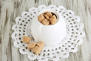 Unrefined sugar in white sugar bowl on wooden background