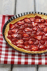 Strawberry tart on checkered red and white table cloth on rustic