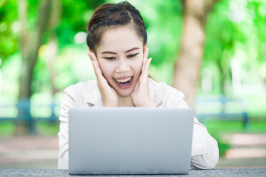 surprised asian girl in front of laptop in park