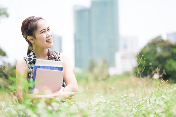Fototapeta premium Young woman sitting on green grass and hug book
