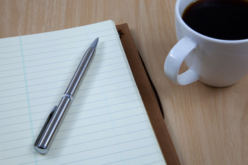 Cup of coffee on a wooden table with book and pen