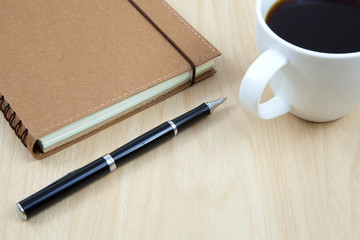 Cup of coffee on a wooden table with book and pen