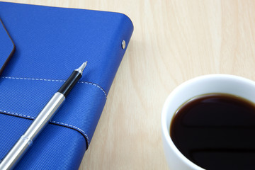 Cup of coffee on a wooden table with book and pen