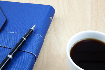 Cup of coffee on a wooden table with book and pen