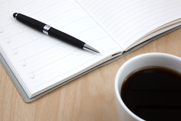 Cup of coffee on a wooden table with book and pen