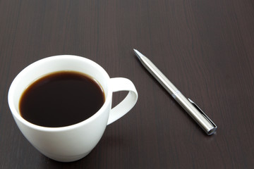 Cup of coffee on a wooden table with pen