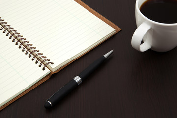 Cup of coffee on a wooden table with book and pen