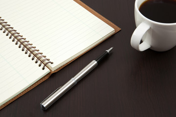 Cup of coffee on a wooden table with book and pen