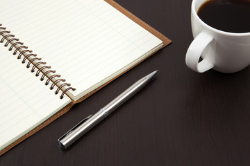 Cup of coffee on a wooden table with book and pen