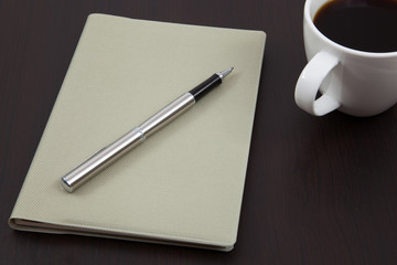 Cup of coffee on a wooden table with book and pen