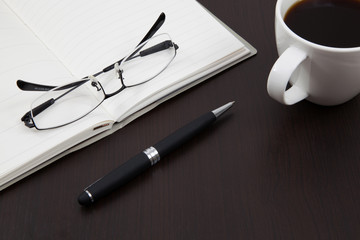 Cup of coffee on a wooden table with book and pen