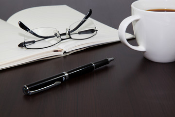 Fototapeta premium Cup of coffee on a wooden table with book and pen