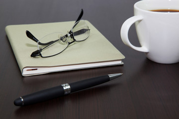 Fototapeta premium Cup of coffee on a wooden table with book and pen