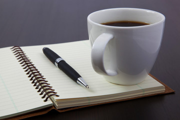 Cup of coffee on a wooden table with book and pen