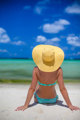 Woman sitting on beach holding beach hat enjoying summer