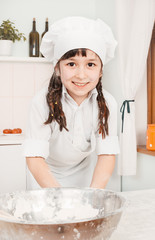 little girl chef preparing dough in the kitchen wearing a hat