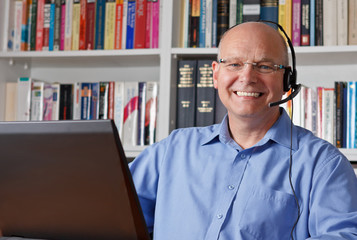 Glücklicher Mann mit Headset vor Laptop in Bibliothek; Textfreiraum.