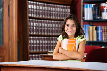 Schoolgirl Holding Book While Sitting At Table In Library