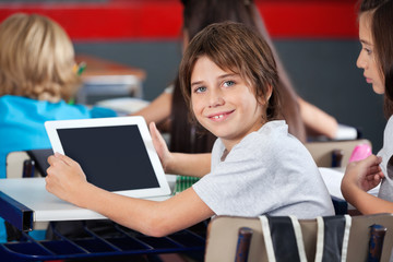 Cute Schoolboy Holding Digital Tablet In Classroom