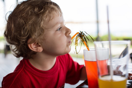 Happy little boy drinking orange juice with straw