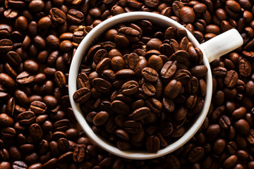 Roasted coffee beans in white cup on wooden background