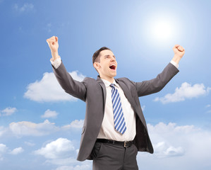 Young satisfied businessman gesturing happiness against blue sky