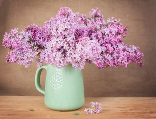 Lilacs in a green jug on a wooden surface